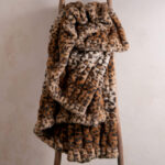 Gradient leopard brown dual-sided elastic bunny faux fur blanket draped over wooden ladder, trendy stretch fuzzy throw