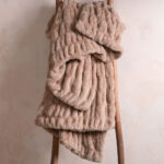 Light brown dual-sided elastic bunny faux fur blanket hanging on wooden ladder, warm stretch plush home throw