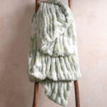 Tie-dye sage green dual-sided elastic bunny faux fur blanket draped over wooden ladder, fresh stretch fluffy bedding